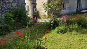 Ein Steinhaus mit einem Ziegeldach, ein kleiner Garten mit roten Klatschmohn und eine hölzerne Bank.