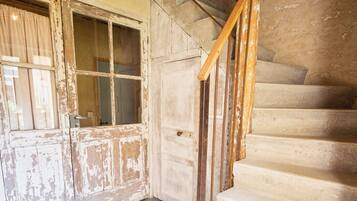 Un intérieur rustique avec un escalier en bois, une porte usée et un luminaire suspendu.