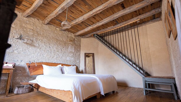 Ein Schlafzimmer mit einem hölzernen Bett, einer Steinwand und einer Holztreppe.
