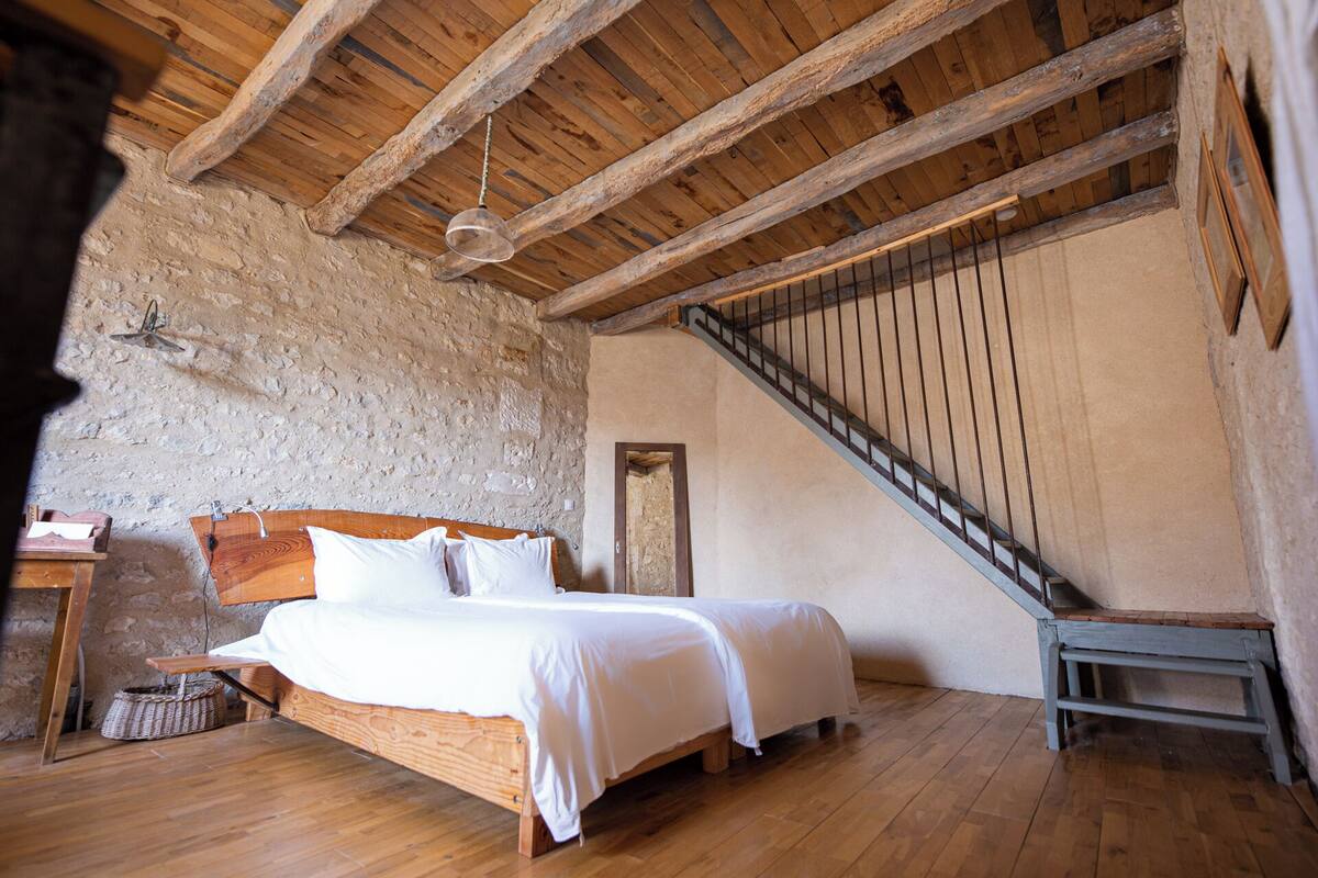 Ein Schlafzimmer mit einem hölzernen Bett, einer Steinwand und einer Holztreppe.