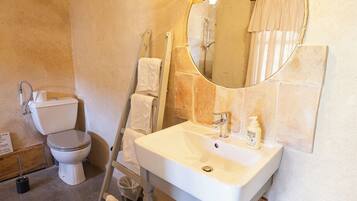 Ein Badezimmer mit weißem Waschbecken, Toilette und Spiegel. Ein Handtuchhalter und eine Duschvorhang sind zu sehen.
