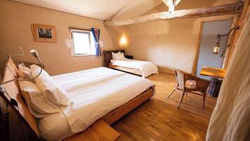 Een slaapkamer met twee bedden, een houten vloer, een raam met gordijnen, een bedlampje en een rieten stoel.