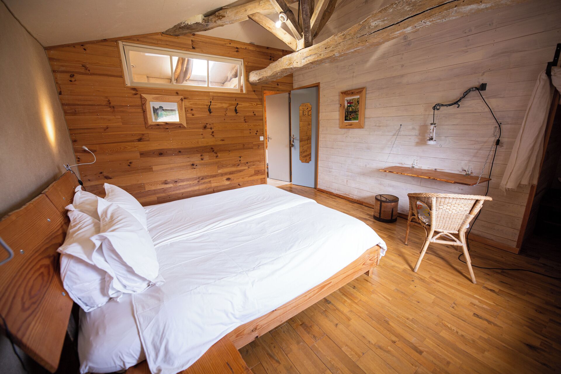 Une chambre dans une cabane en bois, avec un lit, un fauteuil suspendu et une petite table.