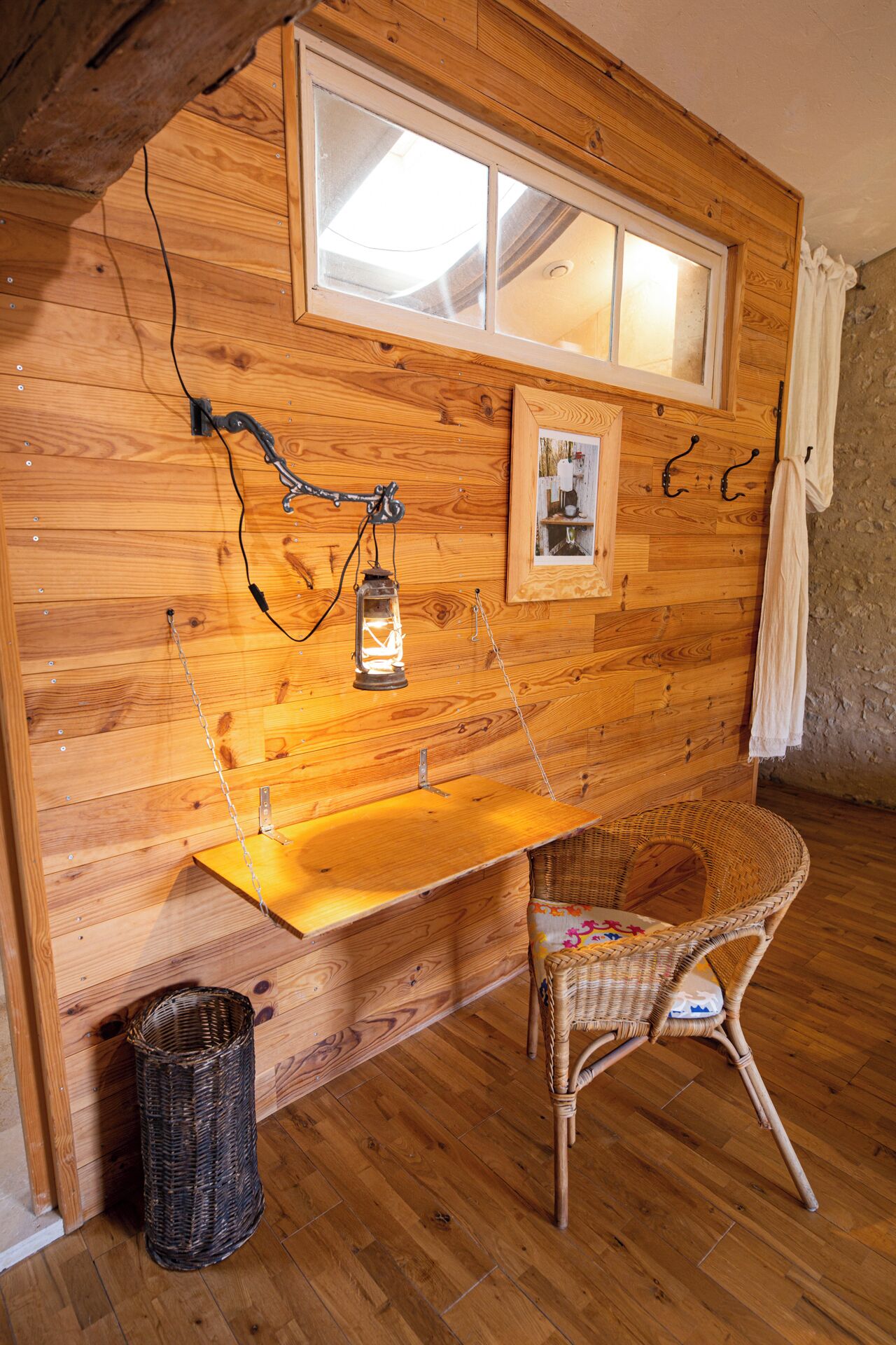 A rustic wooden interior with a wooden bench, a wicker chair, a lantern, and a framed picture on the wall.