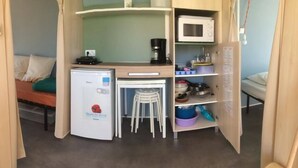 A compact kitchenette with a refrigerator, microwave, coffee maker, and a small dining area with stools. - Ridorev (Auxonne)