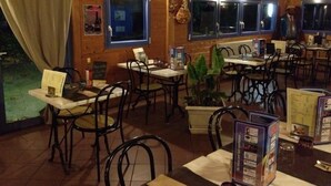 A restaurant interior with wooden walls, black metal chairs, and tables. There are menus on the tables and a plant in the center. - Ridorev (Auxonne)