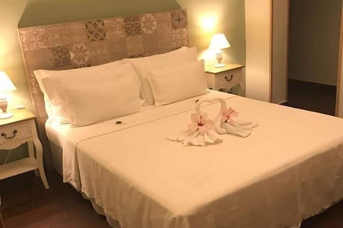 A neatly made bed with white linens and a decorative swan and flowers on the bedspread.