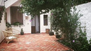 A courtyard with a tiled floor, wicker chairs, potted plants, and a white wall. - Guest House Le Ginestre Dell'Etna (Belpasso)