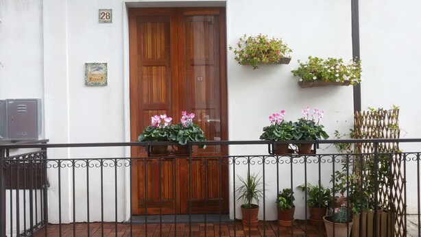 A wooden door with a metal gate in front, potted plants on the balcony, and a small gas meter on the wall. - Guest House Le Ginestre Dell'Etna (Belpasso)