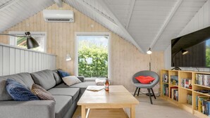 Een gezellige woonkamer met een grijze bank, een houten salontafel, een rode fauteuil en een boekenplank vol boeken.