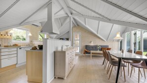 Een ruime keuken met een centraal kookeiland, een eetgedeelte met een grote tafel en stoelen, en een gezellige zithoek met een bank en kussens.