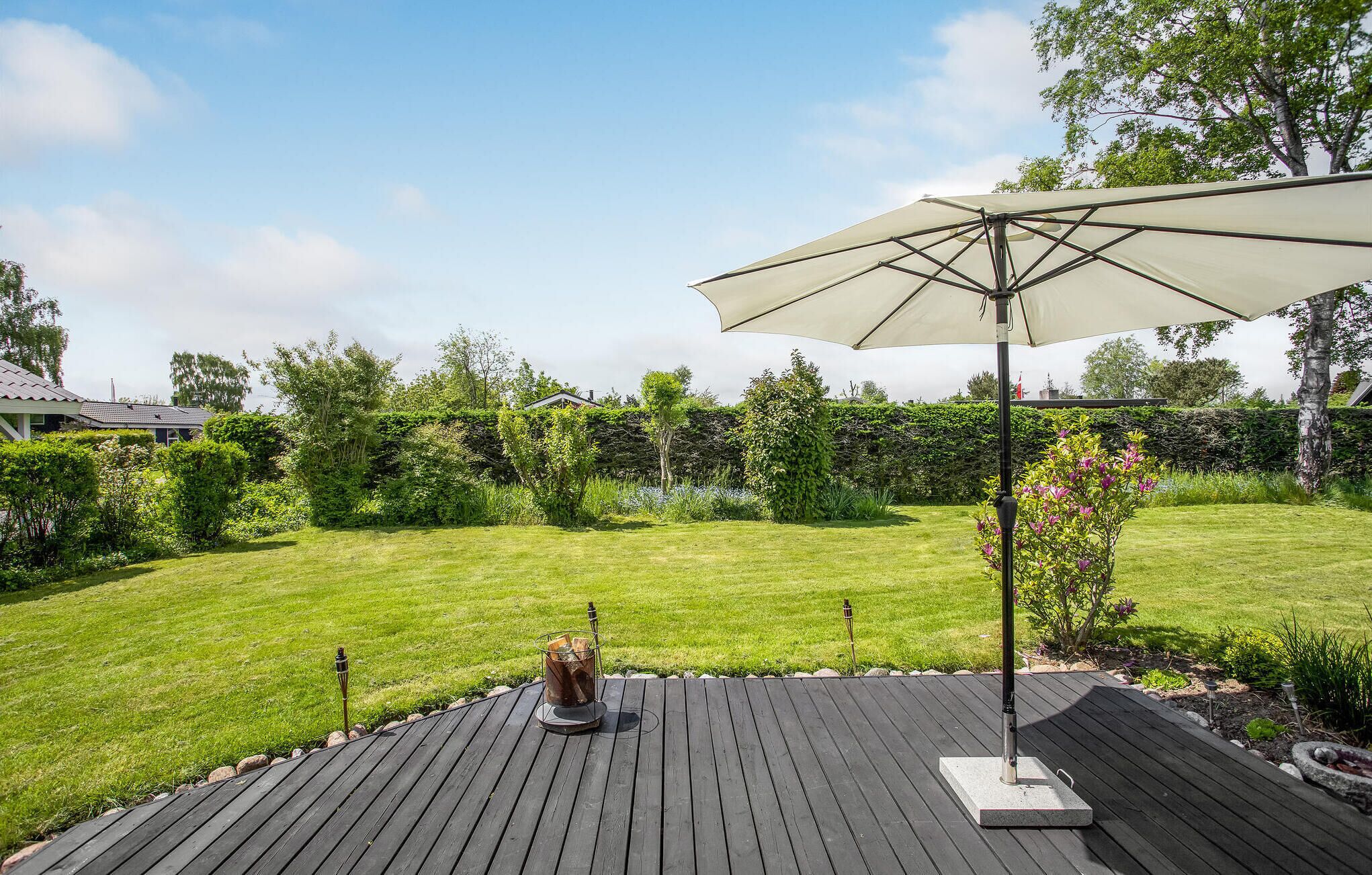 A wooden deck with a large umbrella, surrounded by a well-maintained lawn and various plants.