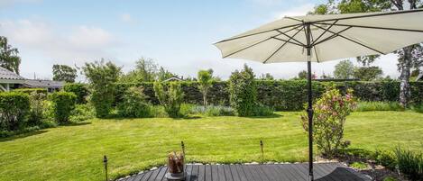 A wooden deck with a large umbrella, surrounded by a well-maintained lawn and various plants.