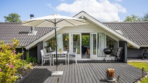 Een overdekt terras met een tafel, stoelen, een barbecue en een pergola.