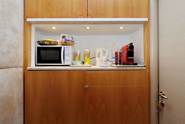 A kitchenette with a microwave, coffee maker, and various food items on the counter.