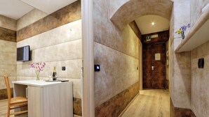A modern hotel room with a wooden floor, a small wooden desk with a vase of flowers, a flat-screen TV mounted on the wall, and a door leading to another room. - Gialli Vatican Guesthouse (Rome)