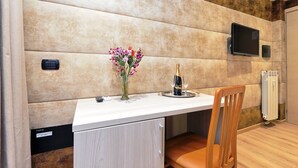 A modern room with a white table, a wooden chair, a vase with flowers, a bottle of champagne, and a TV mounted on the wall. - Gialli Vatican Guesthouse (Rome)