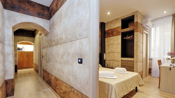 A modern hotel room with a wooden floor, a bed with a beige bedspread, a wardrobe, and a bathroom with a shower and toilet. - Gialli Vatican Guesthouse (Rome)