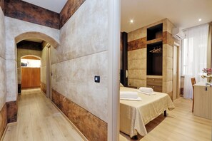 A modern hotel room with a wooden floor, a bed with a beige bedspread, a wardrobe, and a bathroom with a shower and toilet.