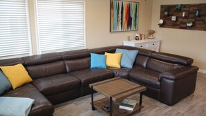 A living room with a brown leather sectional sofa, a wooden coffee table, and a white side table with decorative items. - Well-Furnished Oceanside Home! (Pismo Beach)