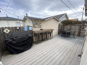 En trädgård med en träaltan, en grill, ett matbord med stolar och en barhörna med barstolar.