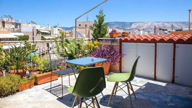 Una terrassa al terrat amb taula i cadires, plantes en testos i vistes a la ciutat.