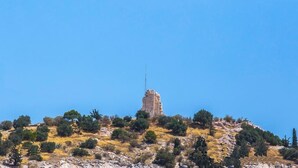Edifici de pedra en un turó amb vegetació escassa i cel serè.