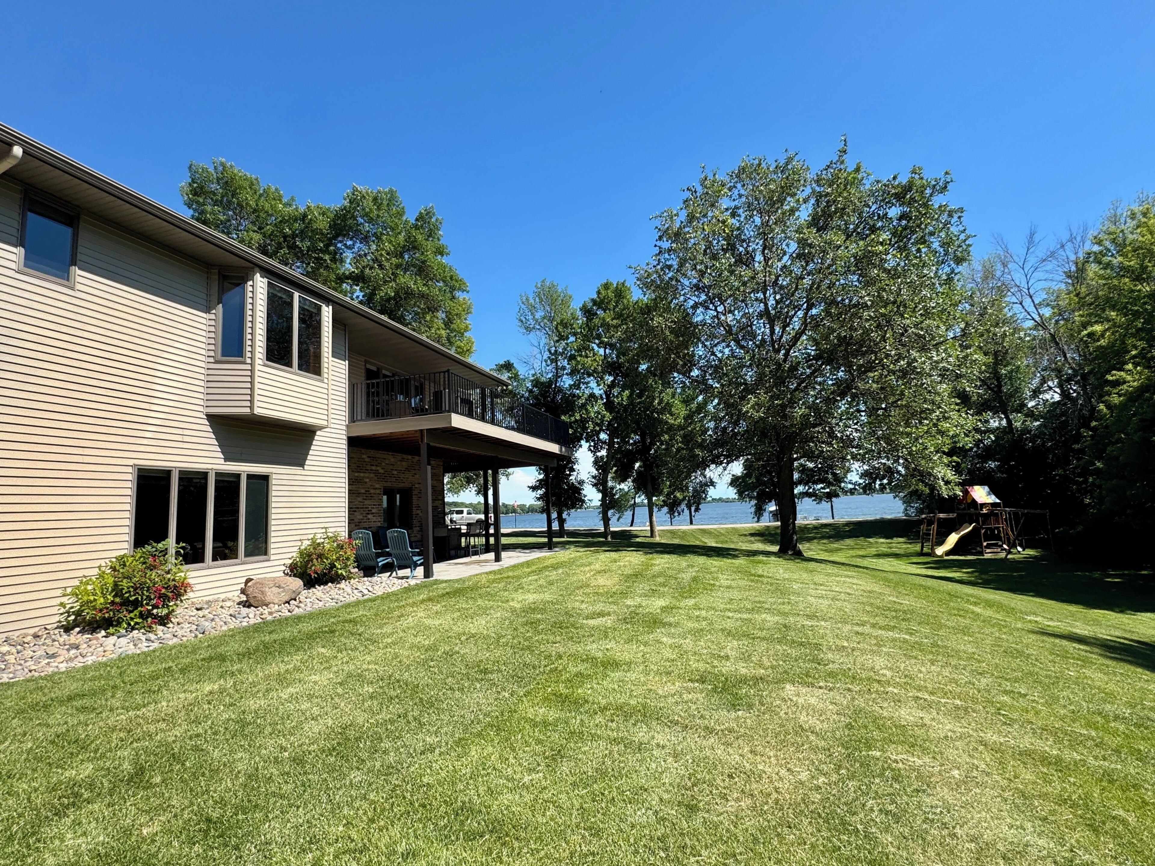 Une maison à deux étages dotée d’un patio couvert et offrant une vue sur un lac.