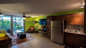 A compact kitchen with a refrigerator, wooden cabinets, and a dining area with a table and chairs. - Oceanfront Remodeled Studio Condo (Kailua-Kona)