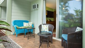 A covered patio area with wicker furniture, a small table, and a sliding glass door leading to an interior space. - Oceanfront Remodeled Studio Condo (Kailua-Kona)
