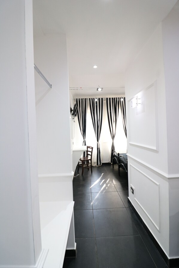 A hallway with white walls, dark tiled flooring, and a chair in the distance.