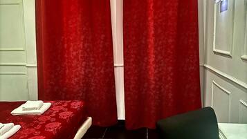 Una habitación con dos camas, cortinas rojas, una silla negra y un televisor montado en la pared.