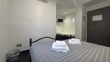 Habitación de hotel con cama, aire acondicionado de pared, un cesto de basura pequeño y una puerta con un cartel.