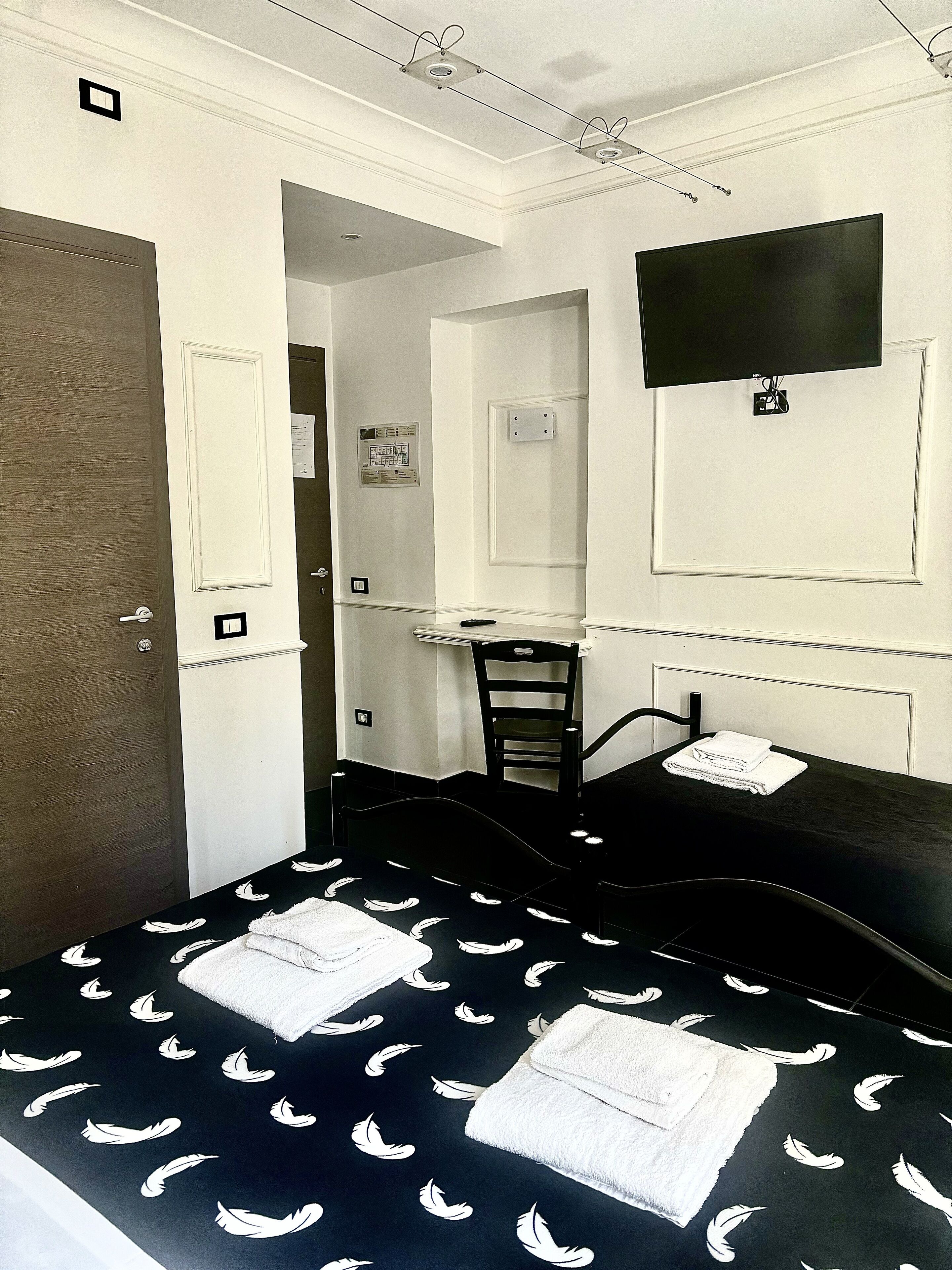 Una habitación de hotel con cama, escritorio, silla y televisor fijado a la pared.