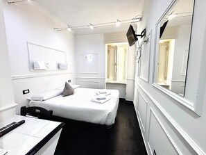 A hotel room with a bed, a desk, a mirror, and a window.