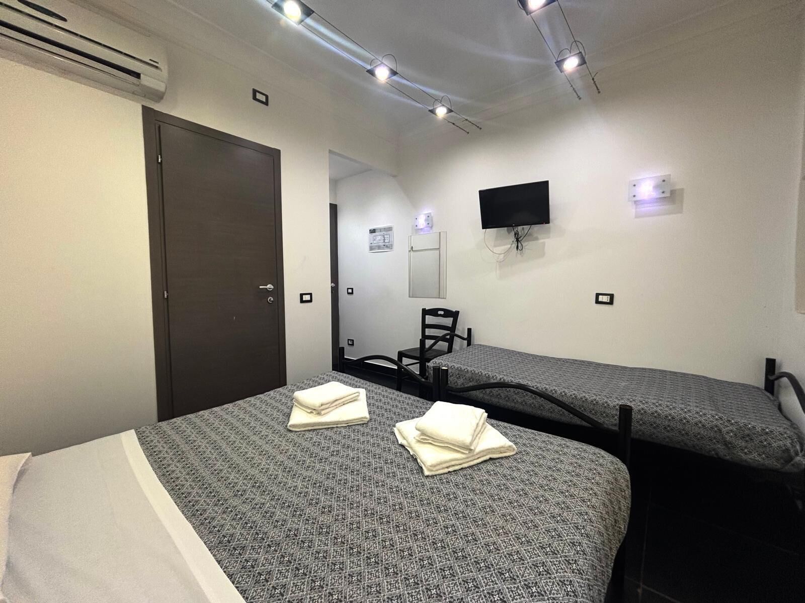 Una habitación de hotel con dos camas individuales, un televisor montado en la pared, una silla y una puerta.