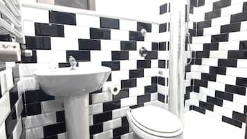 Un baño con salpicadero de azulejos a cuadros blanco y negro, un lavamanos pedestal blanco, un inodoro y una ducha con cabezal de ducha de mano.