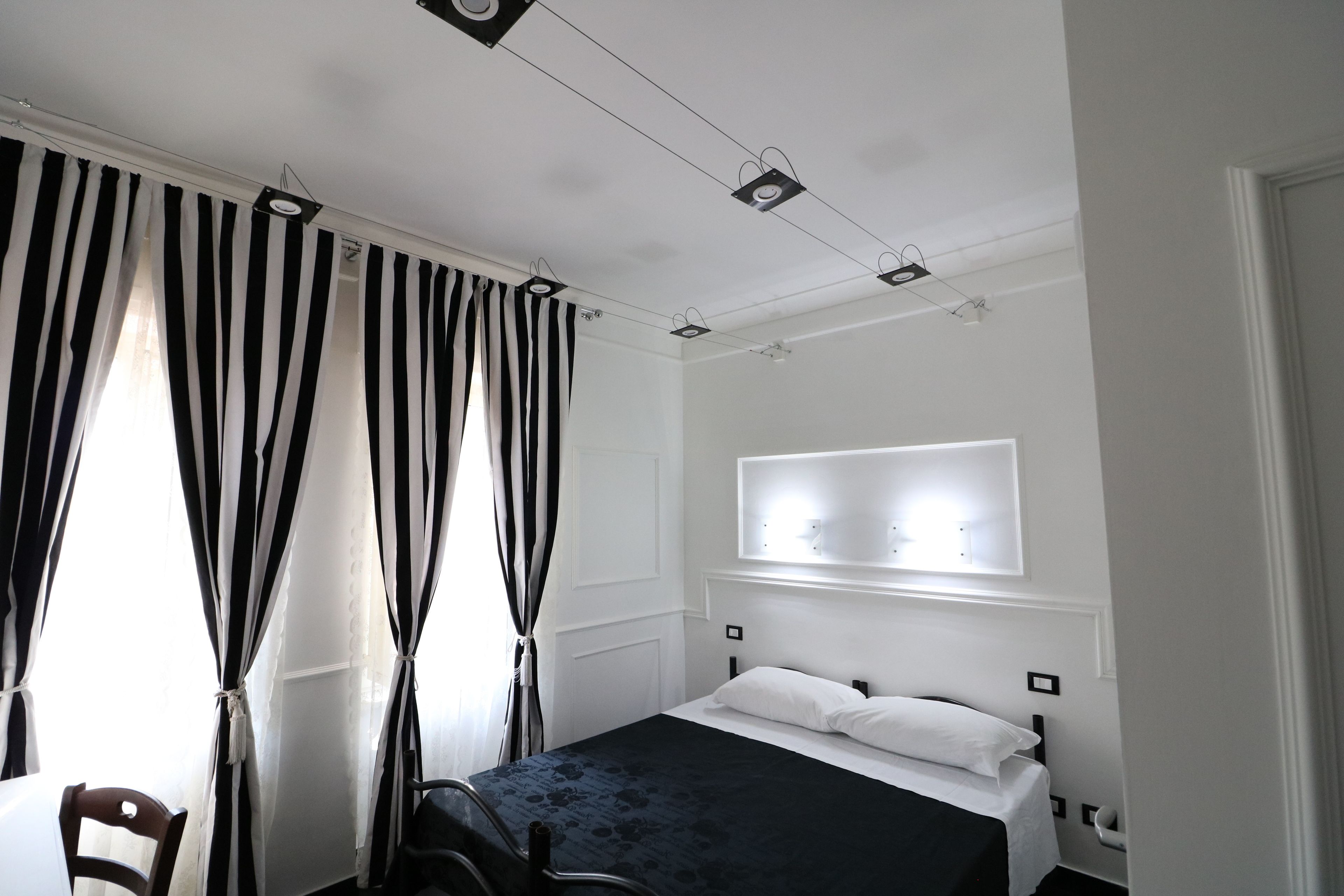 Een hotelkamer met een bed, een stoel, een raam met gordijnen en een wandlamp.