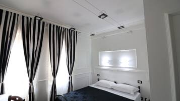 Een hotelkamer met een bed, een stoel, een raam met gordijnen en een wandlamp.