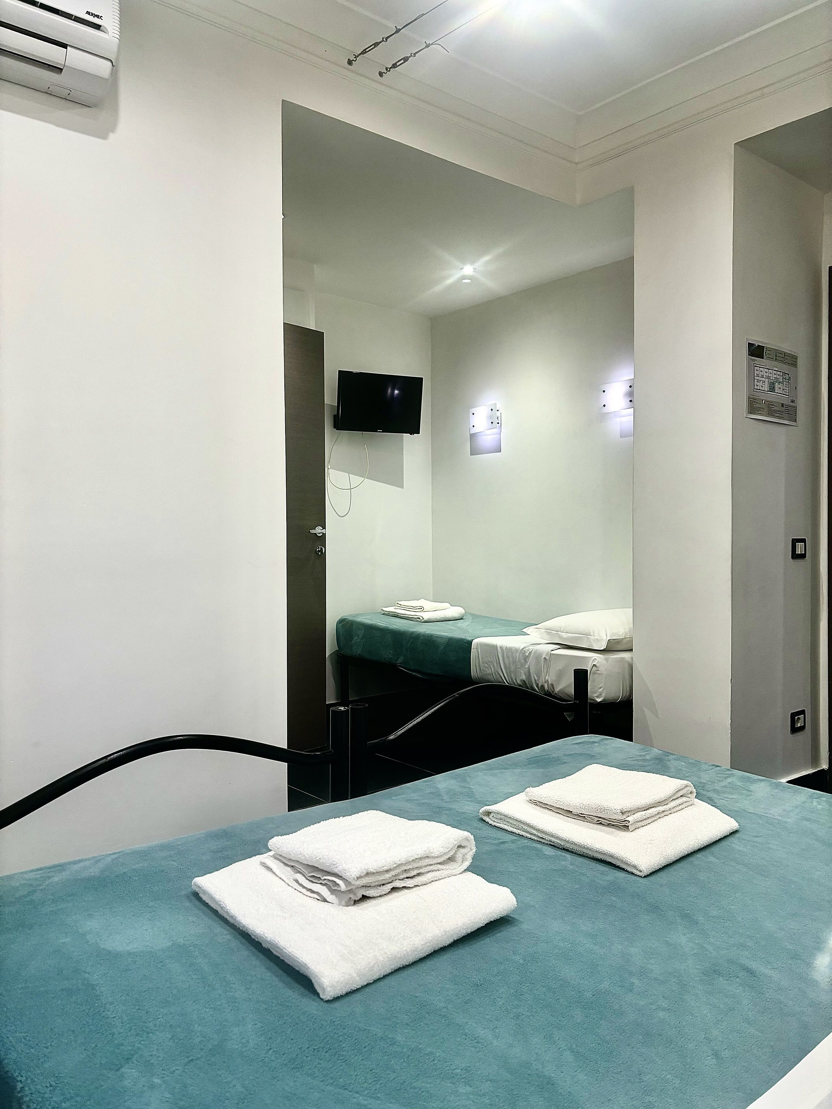 A hotel room with a bed, a TV mounted on the wall, and a table with towels.