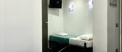 A hotel room with a bed, a TV mounted on the wall, and a table with towels.