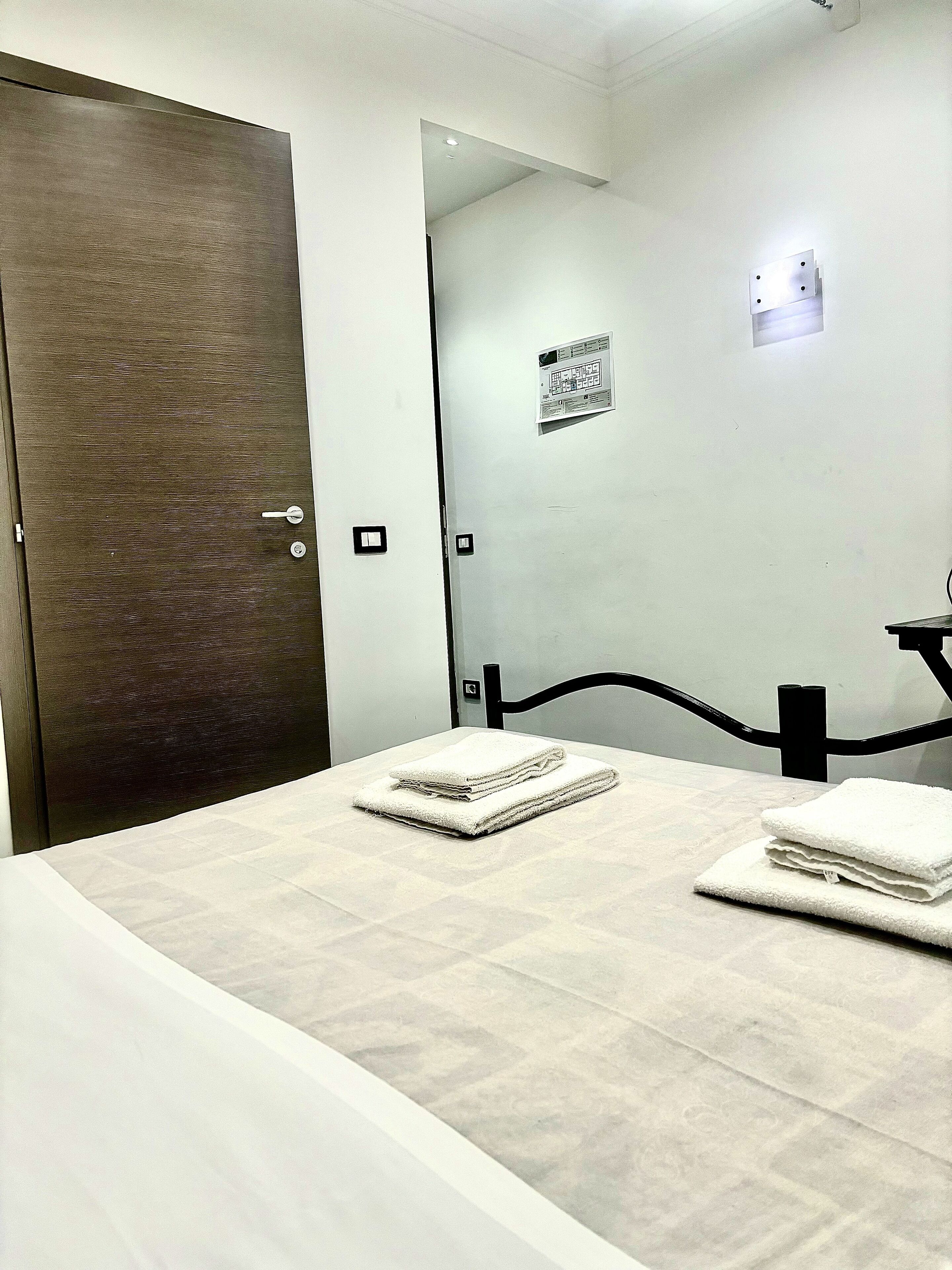 Ein Hotelzimmer mit einem Bett, einer Holztür, einem kleinen Tisch und einer Wandleuchte.
