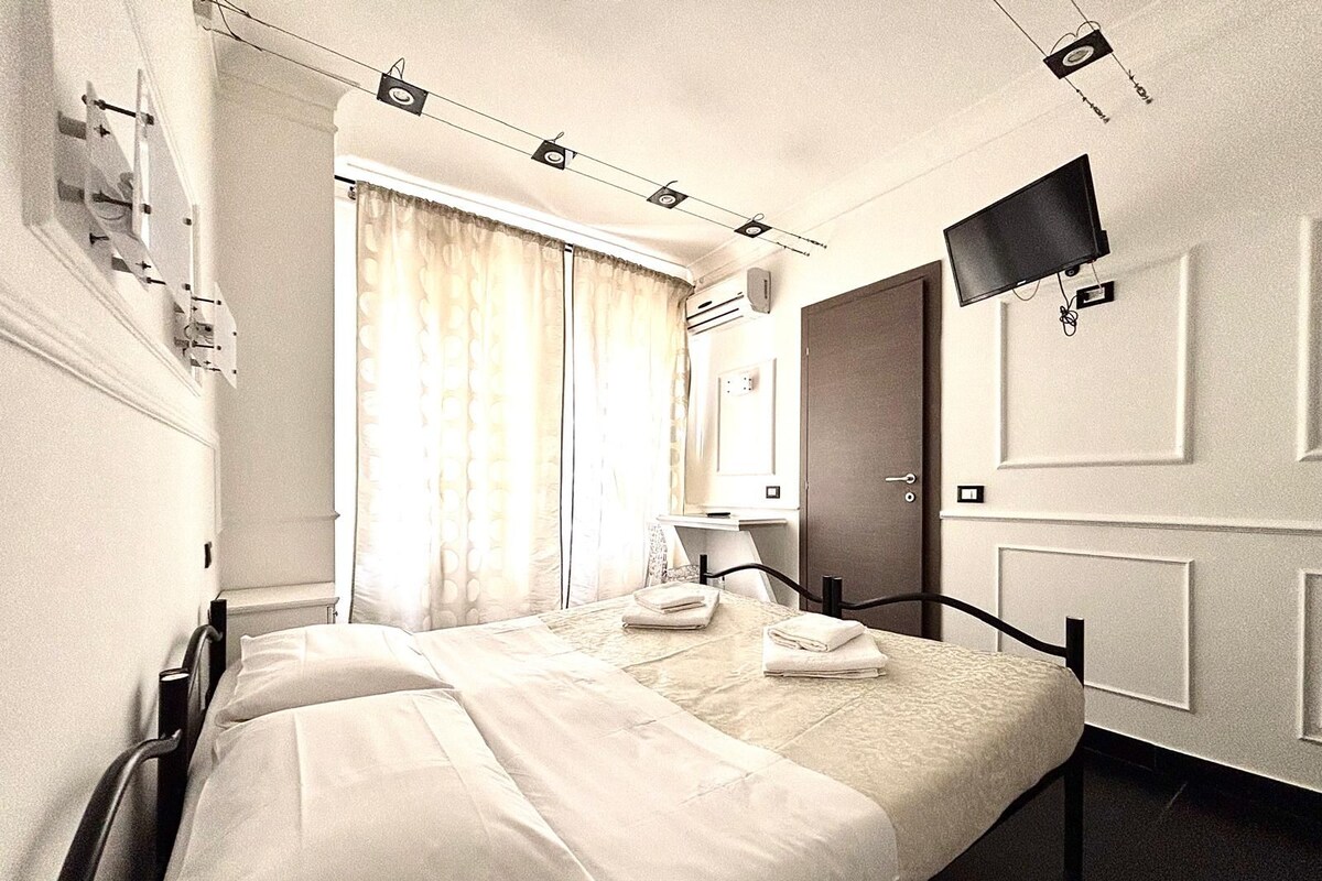 Una habitación de hotel con una cama, un televisor de pantalla plana en la pared, una ventana con cortinas y una puerta.