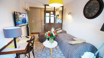 A compact hotel room with a bed, a desk with a chair, a TV, a mirror, and a clock on the wall.