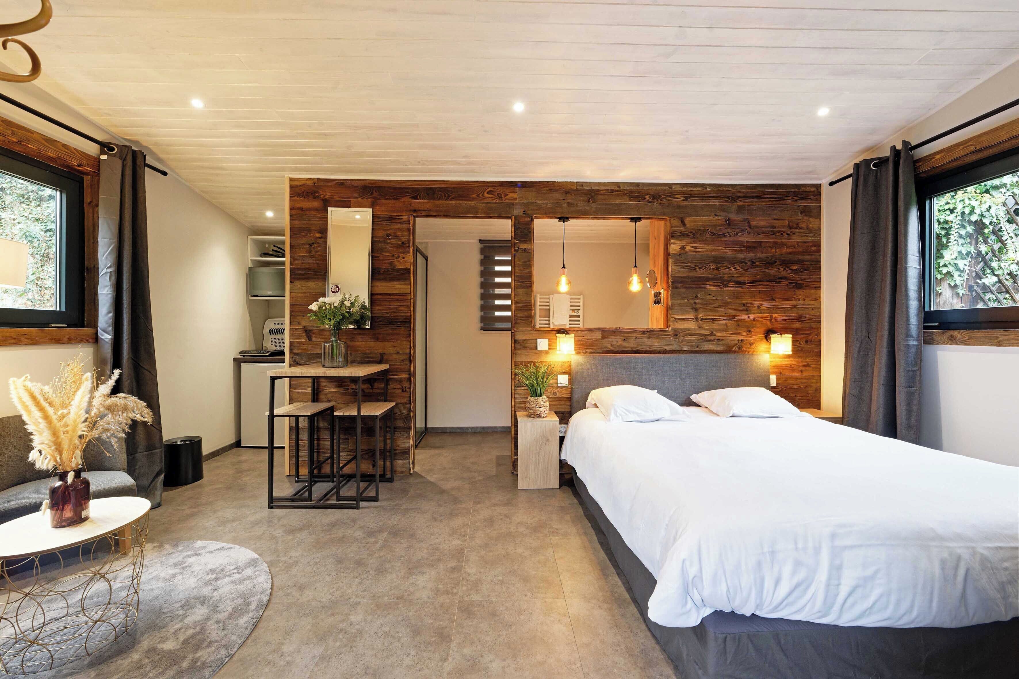 Een moderne slaapkamer met een houten accentmuur, een groot bed, een bureau met stoel, en een kleine tafel met een vaas.