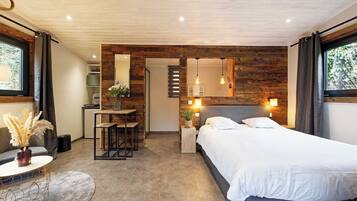 Een moderne slaapkamer met een houten accentmuur, een groot bed, een bureau met stoel, en een kleine tafel met een vaas.