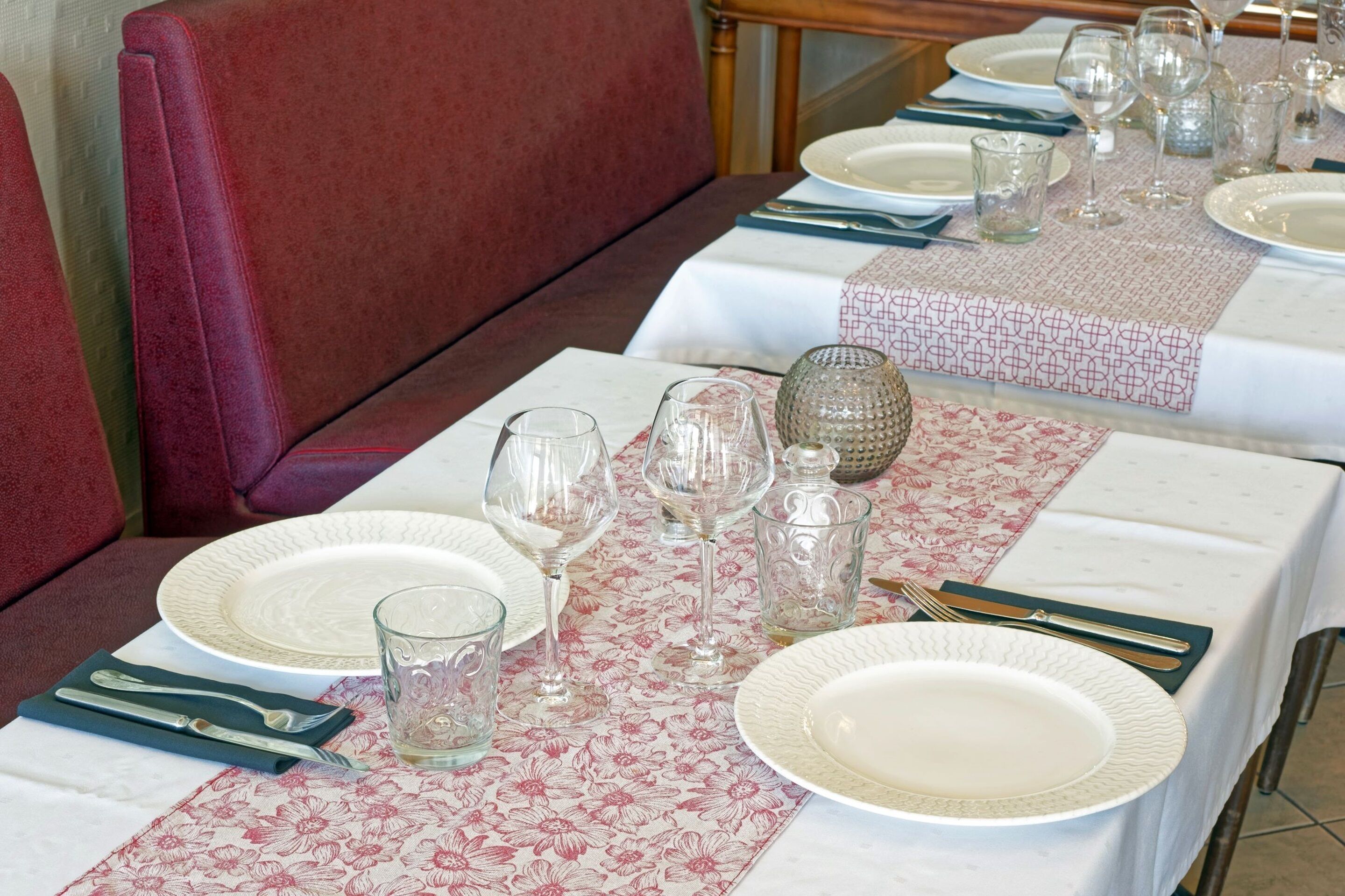 A dining table set with plates, glasses, and cutlery, covered by a patterned table runner.