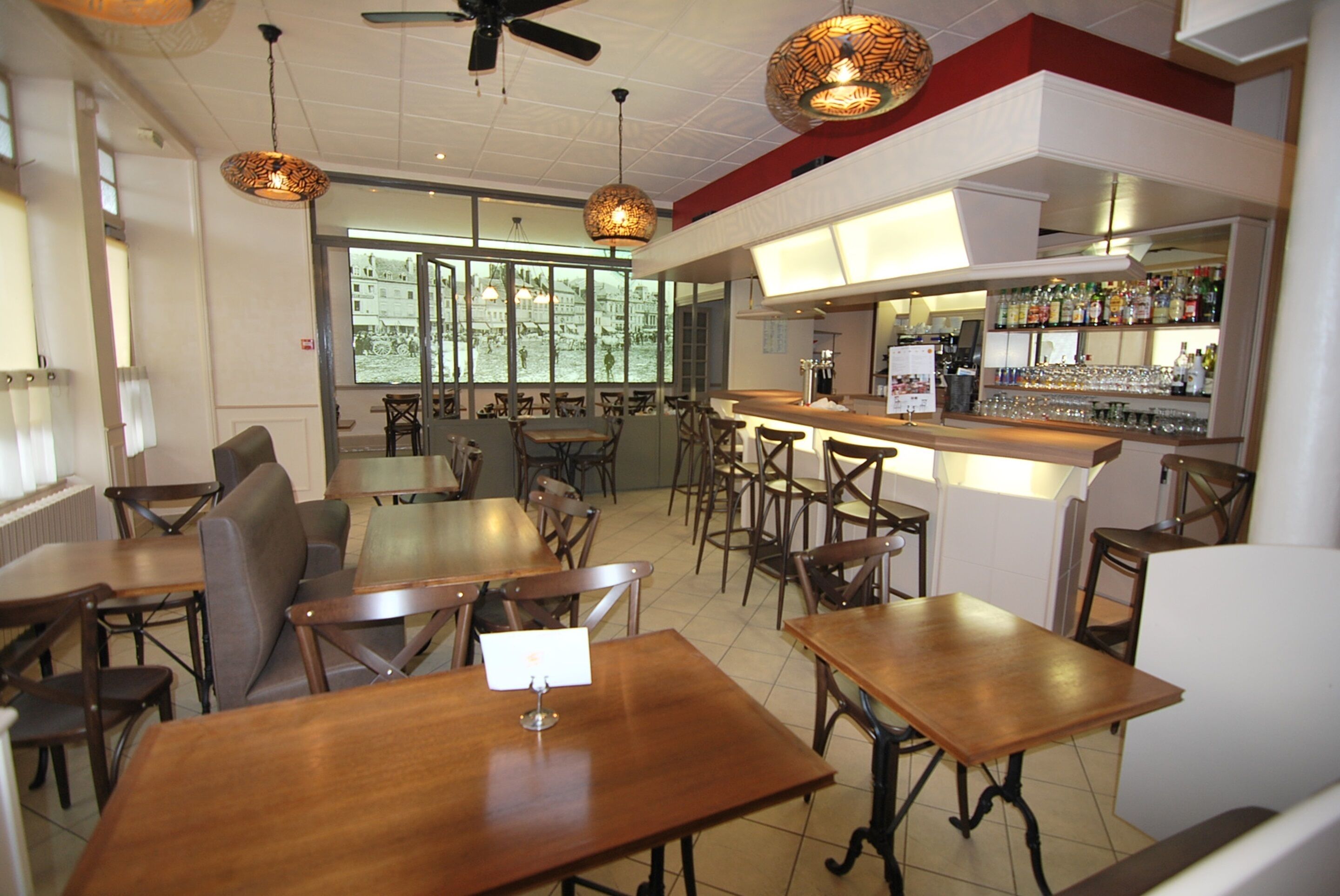 A restaurant with wooden tables and chairs, a bar area with bottles, and large windows offering a view.