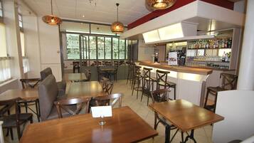 A restaurant with wooden tables and chairs, a bar area with bottles, and large windows offering a view.