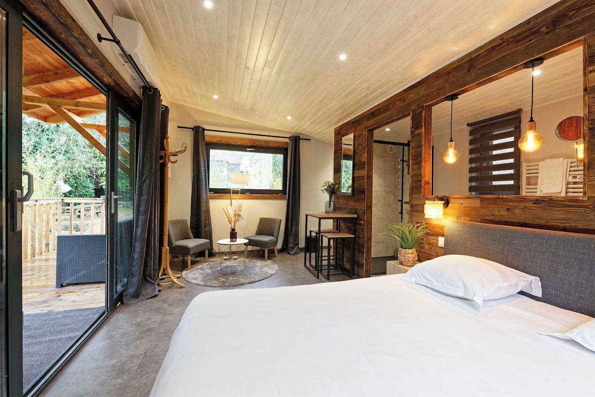 Un dormitorio con una cama grande, techo de madera, un espejo amplio y vistas al exterior.